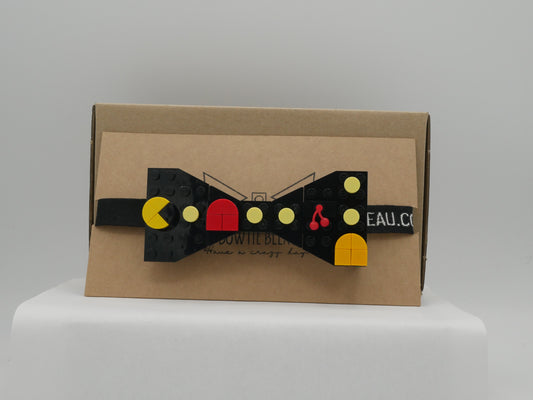 A black LEGO® Retro Arcade Maze Bow Tie with a strap, featuring yellow, orange, red, and cherry LEGO® parts on a cardboard box.